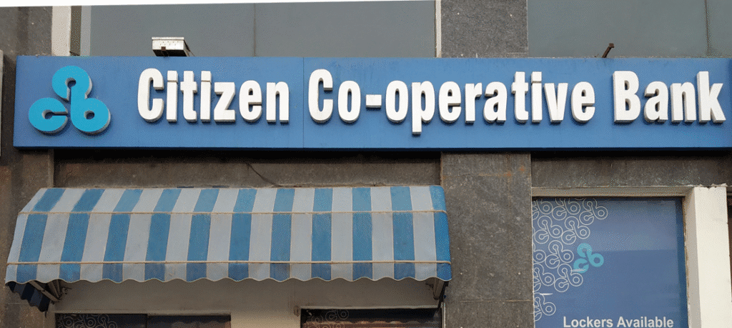 "Citizen Co-operative Bank signboard displaying the bank’s name with a blue and white color scheme, located outside a branch with lockers available for customers."