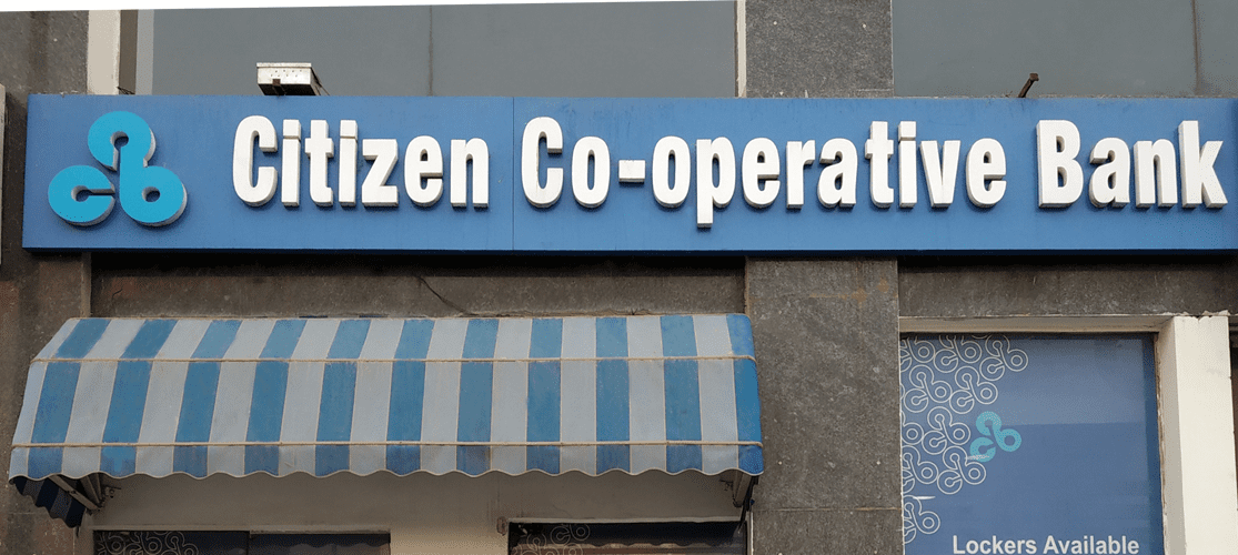 "Citizen Co-operative Bank signboard displaying the bank’s name with a blue and white color scheme, located outside a branch with lockers available for customers."
