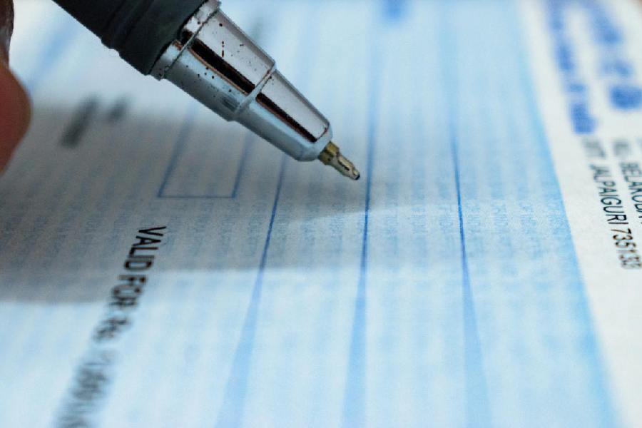 Close-up of a pen writing on a blue Indian bank cheque, with the text "VALID FOR" visible on the cheque.